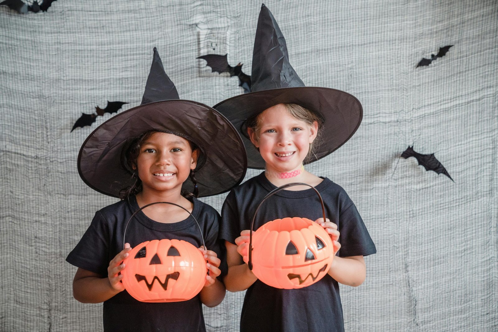 Two girls in witch hats holding pumpkin buckets smile for the camera.